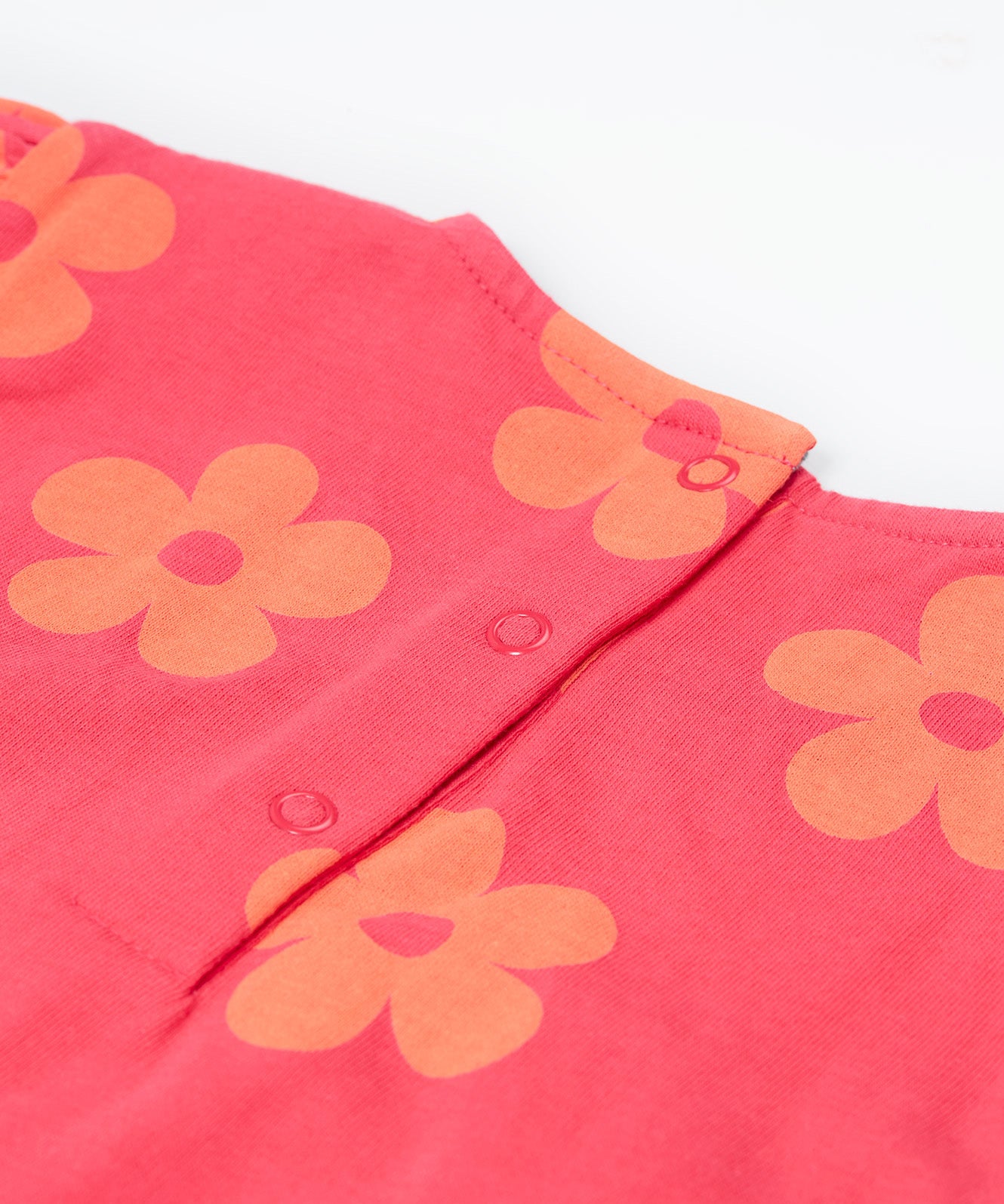 A close up of the Frugi little Lola floral fun / horse dress. Showing the popper fasteners on the back for easy fitting surrounded with light orange printed flowers on a pink organic cotton fabric