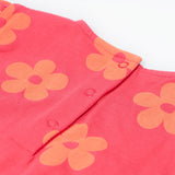 A close up of the Frugi little Lola floral fun / horse dress. Showing the popper fasteners on the back for easy fitting surrounded with light orange printed flowers on a pink organic cotton fabric