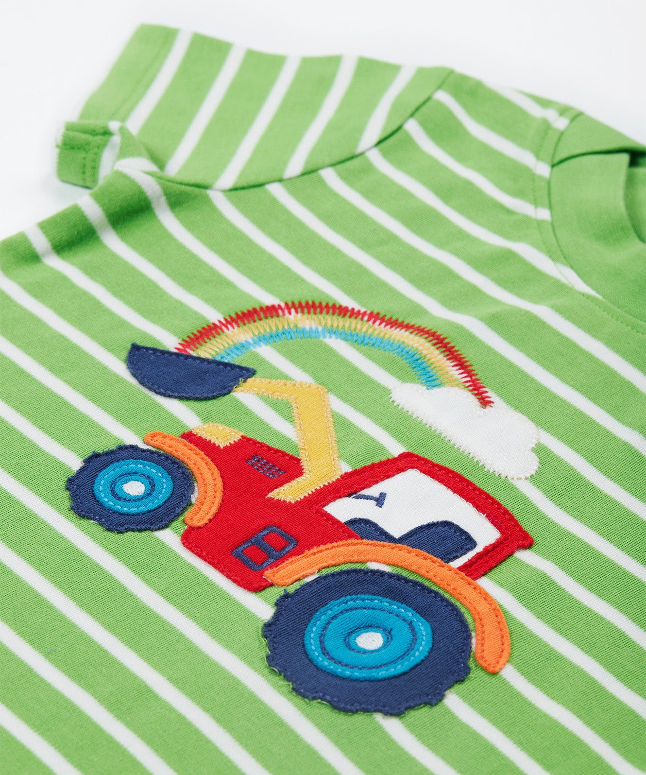 A close up of the Frugi kids breton easy on tractor jumper. Showing a short sleeve, green neck trim, red tractor applique and a rainbow embroidery on green and white stripe organic cotton fabric