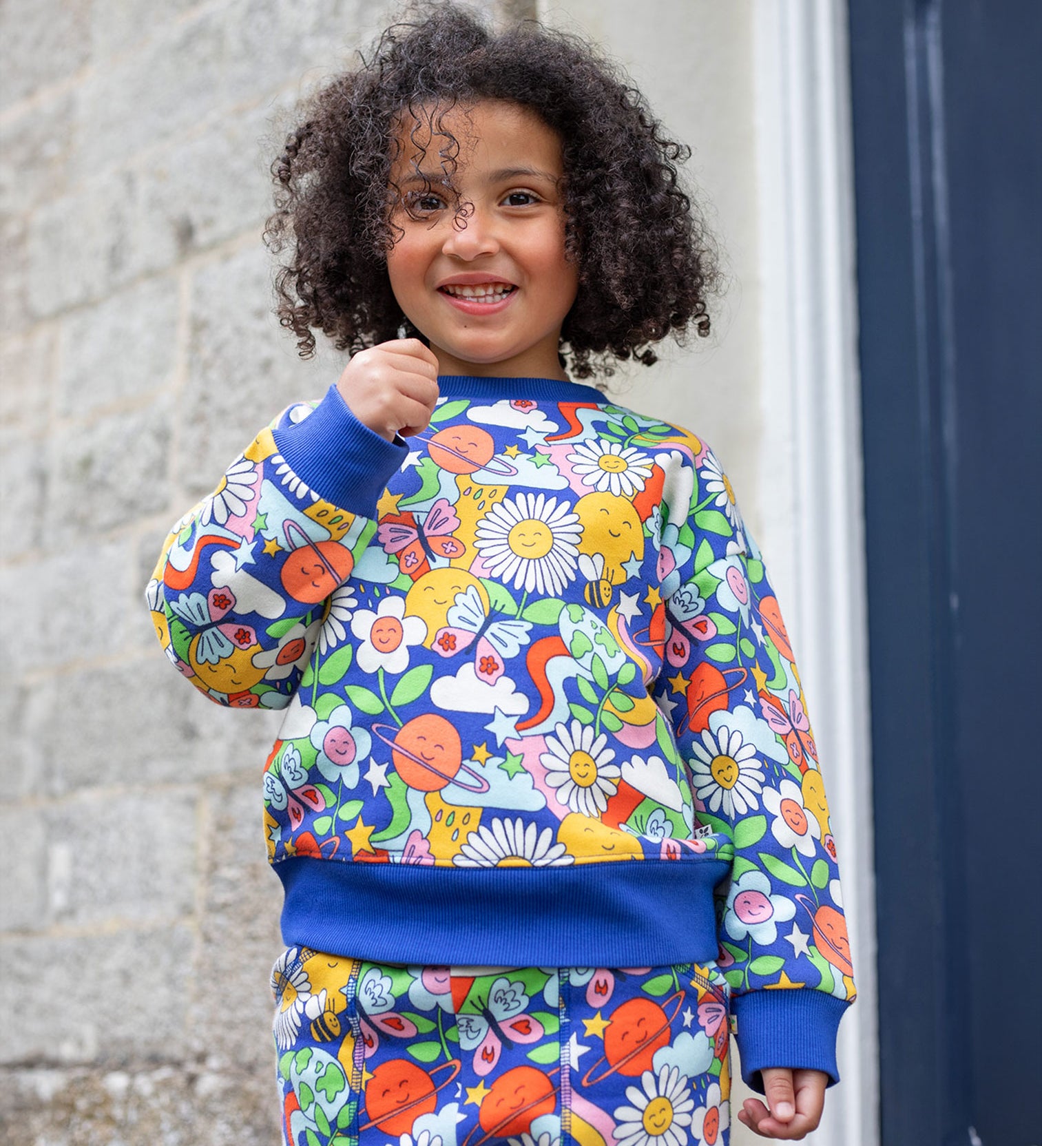 A child wearing the Frugi Easy On kids Jumper with a Retro Happy print with the matching trousers. 