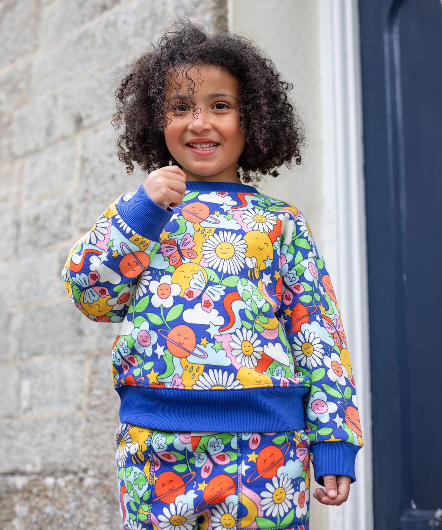 A child wearing the Frugi Easy On kids Jumper with a Retro Happy print with the matching trousers. 