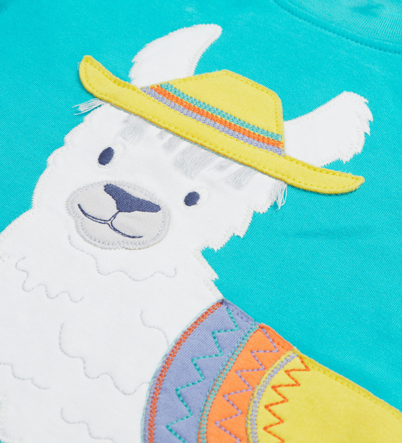 Close up of the Frugi kids easy on llama outfit. Showing the detail of the grey llama wearing a yellow hat with a purple orange and yellow saddle. Features loose cotton threads to represent hair on blue organic cotton fabric