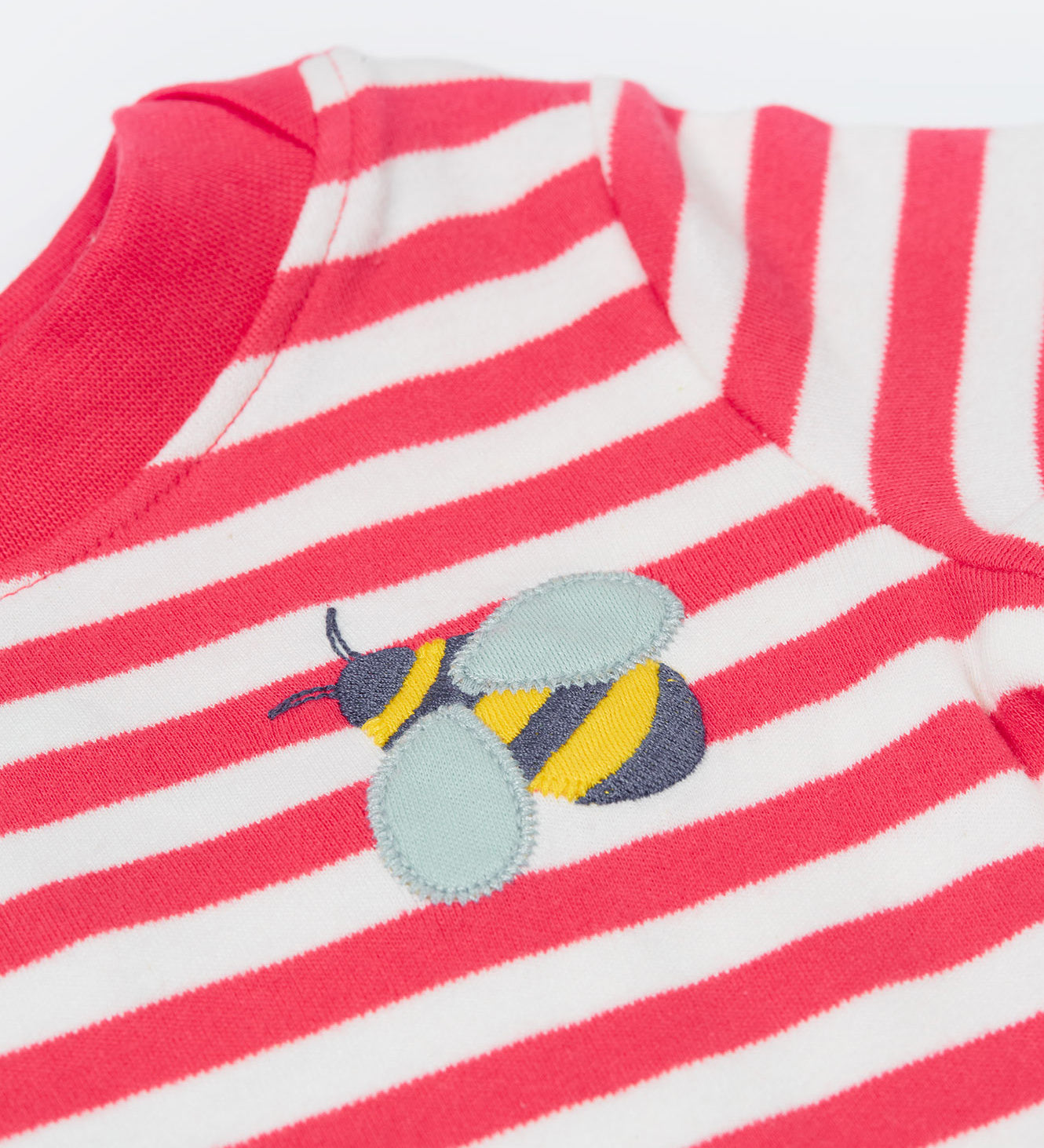 A close up of the t-shirt from the Frugi kids bee stripe outfit. Showing the bee applique with light grey wings on a light pink and white striped organic cotton fabric