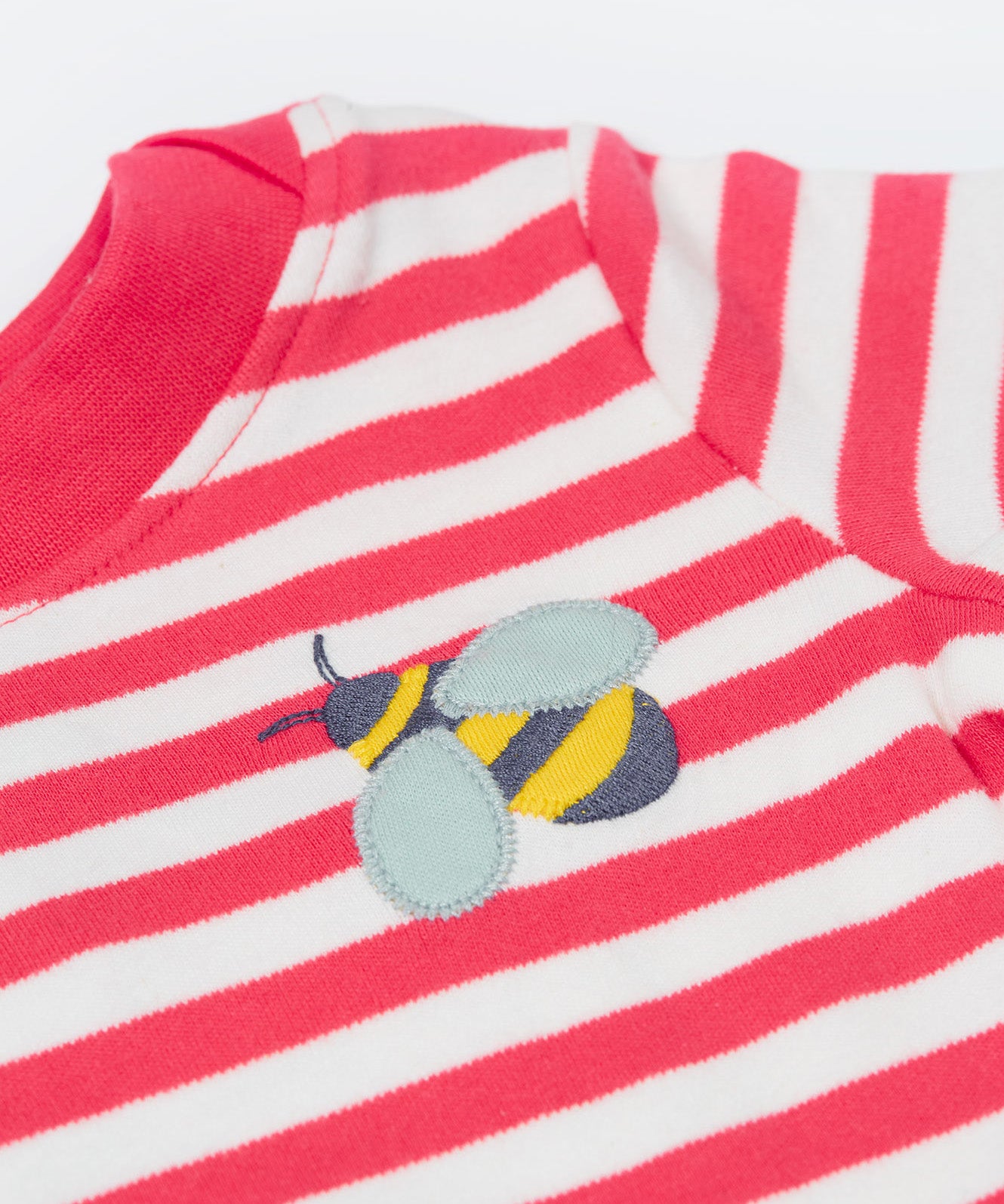 A close up of the t-shirt from the Frugi kids bee stripe outfit. Showing the bee applique with light grey wings on a light pink and white striped organic cotton fabric