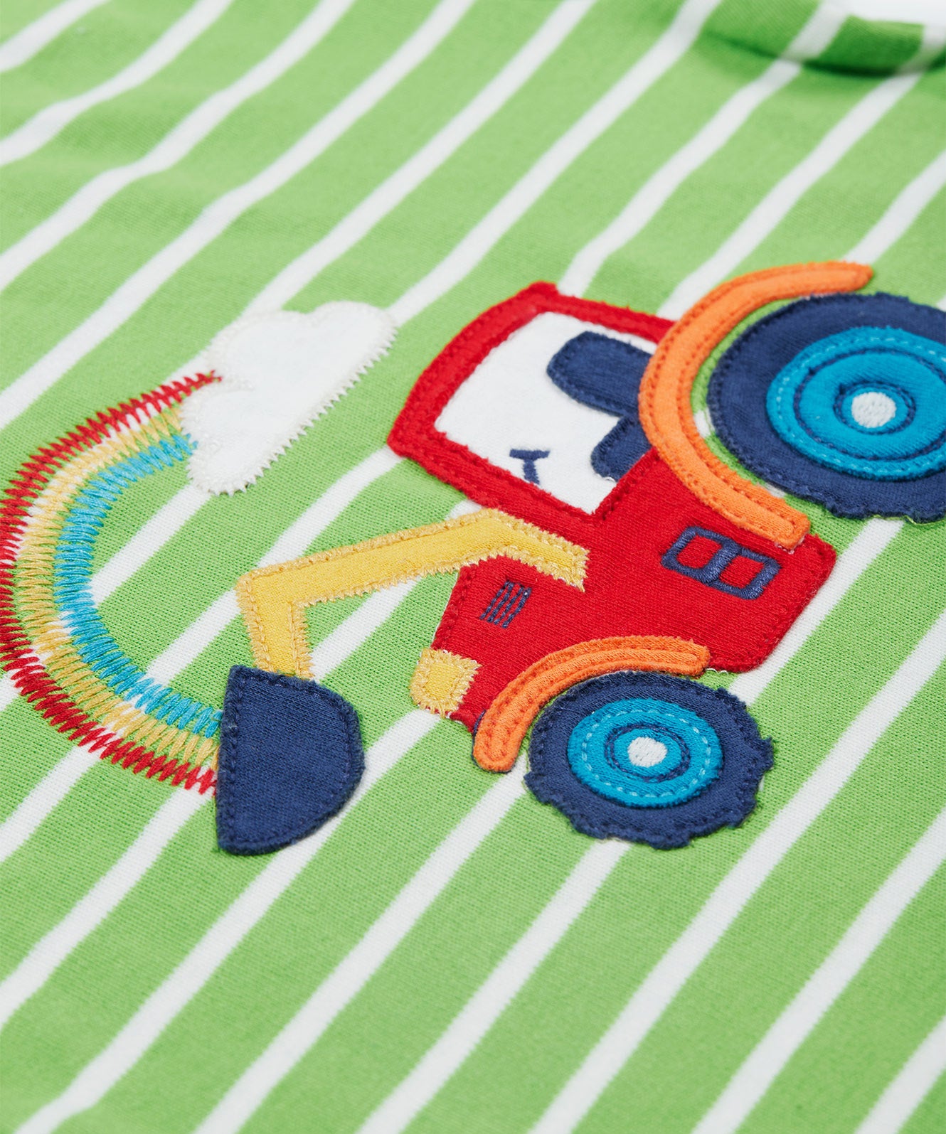 A close up of the Frugi kids breton easy on tractor jumper. Showing a red tractor applique and a rainbow embroidery on green and white stripe organic cotton fabric