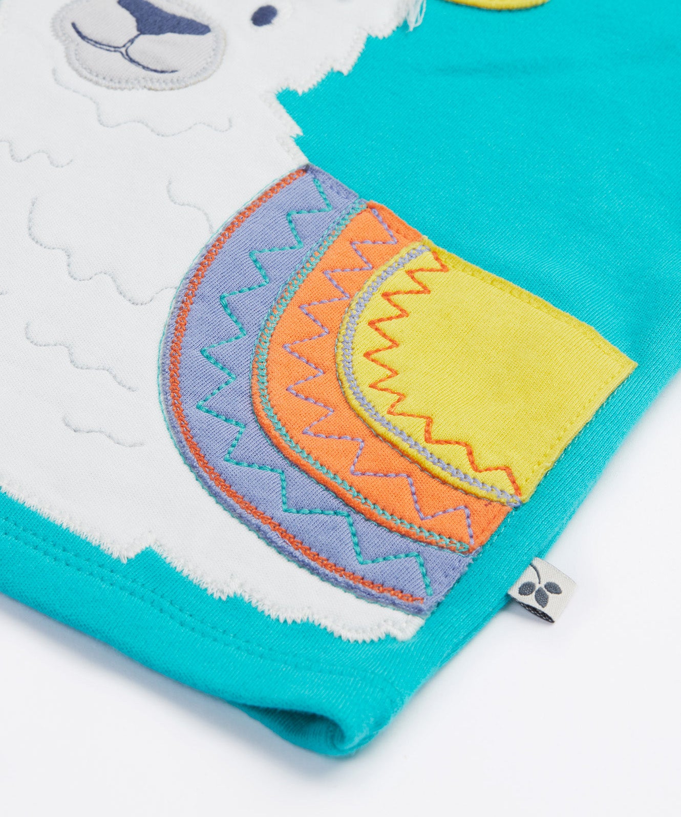 Close up of the Frugi kids easy on llama outfit. Showing the detail of the grey llama with a purple orange and yellow saddle. Features loose cotton threads to represent hair on blue organic cotton fabric