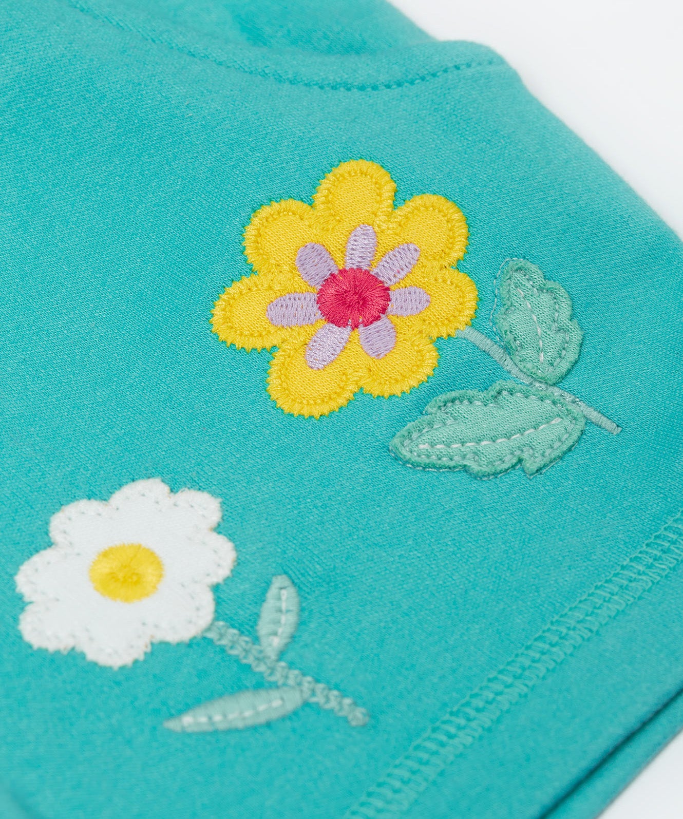 A close up of the shorts from the Frugi kids bee stripe outfit. Showing the flowers applique on a light blue organic cotton fabric