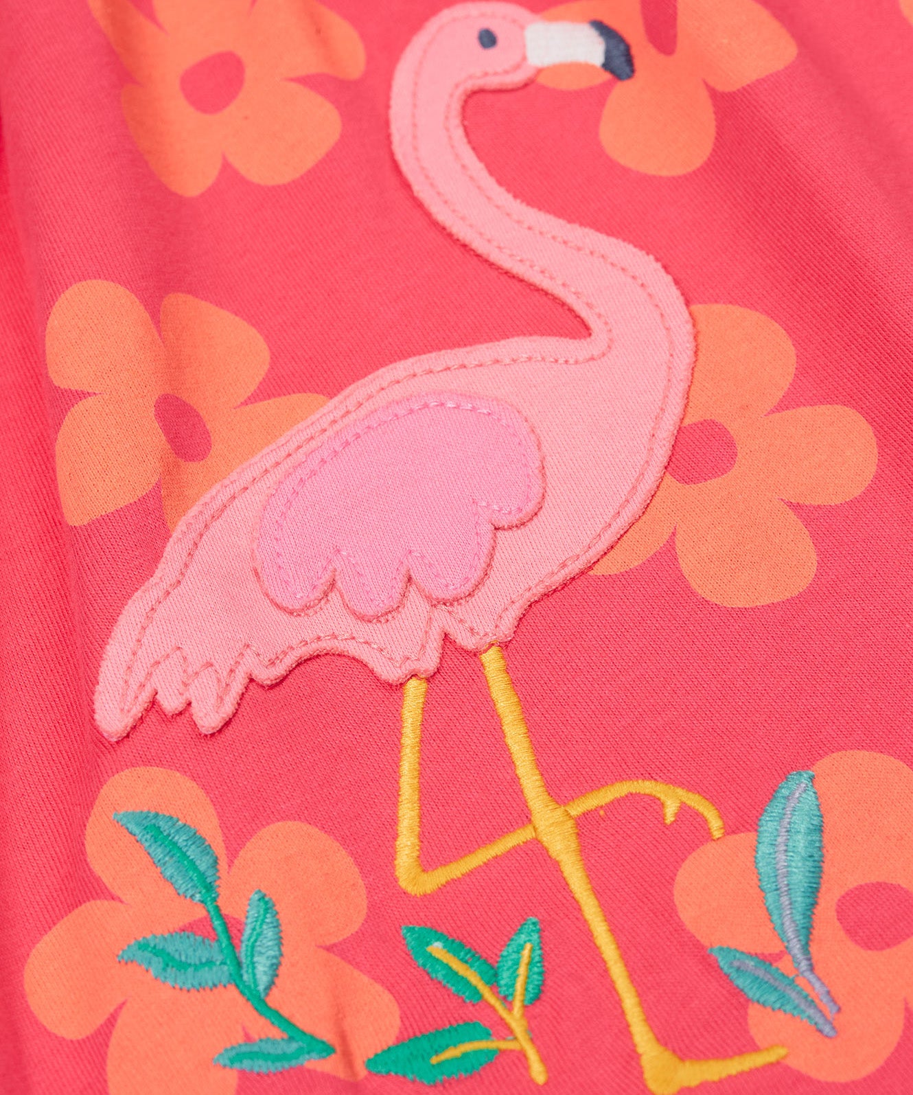 A close up of the Frugi kids summer flamingo / flower dress. Showing the detail of the pink flamingo appliqué with the light coral flowers print surrounding the flamingo on pink organic cotton fabric