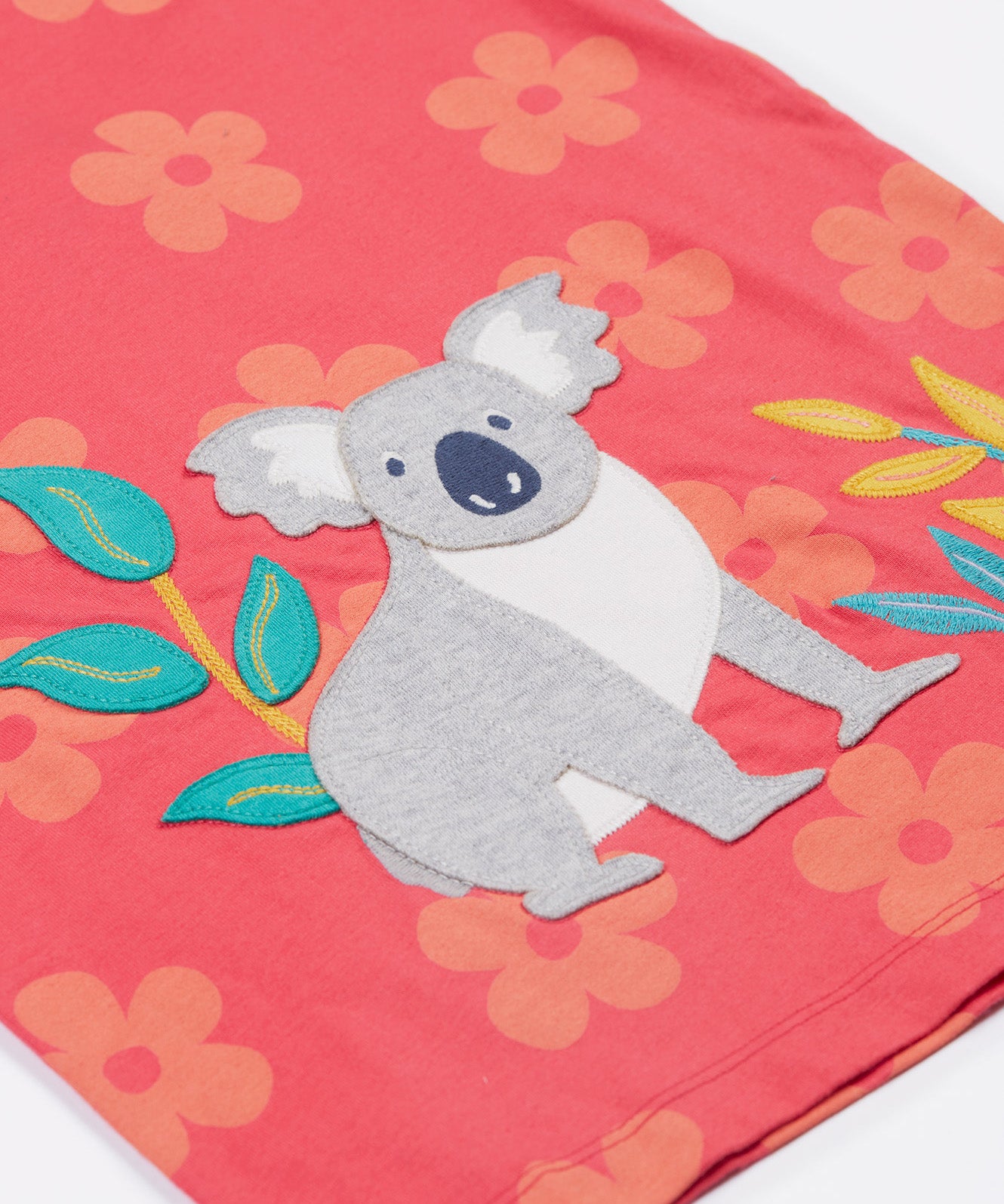 Close up of the Frugi kids flora fun koala t-shirt. Showing the appliqué of the grey koala next to coloured leaves on light pink organic cotton fabric with pastel orange floral prints