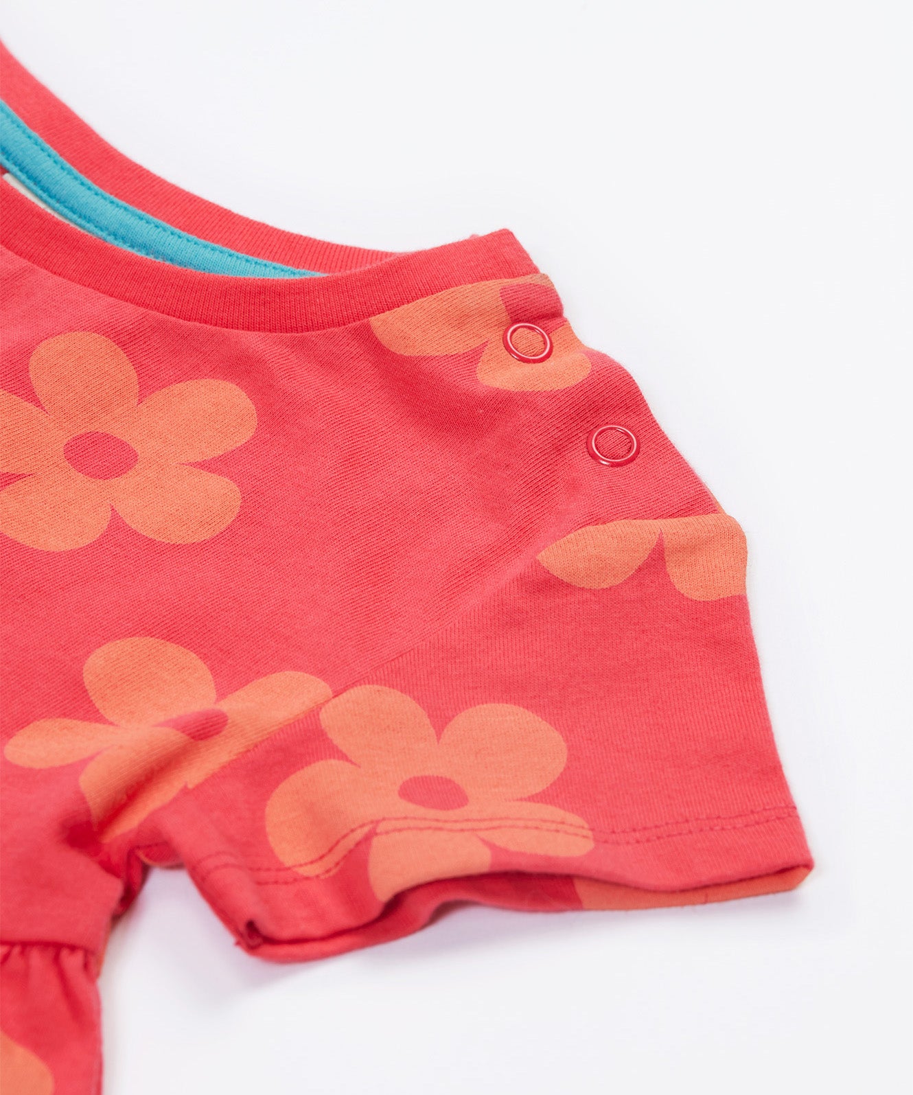 Close up of the Frugi kids flora fun koala tunic top. Showing the two popper fastener detail on the shoulder on light pink organic cotton fabric with pastel orange floral prints