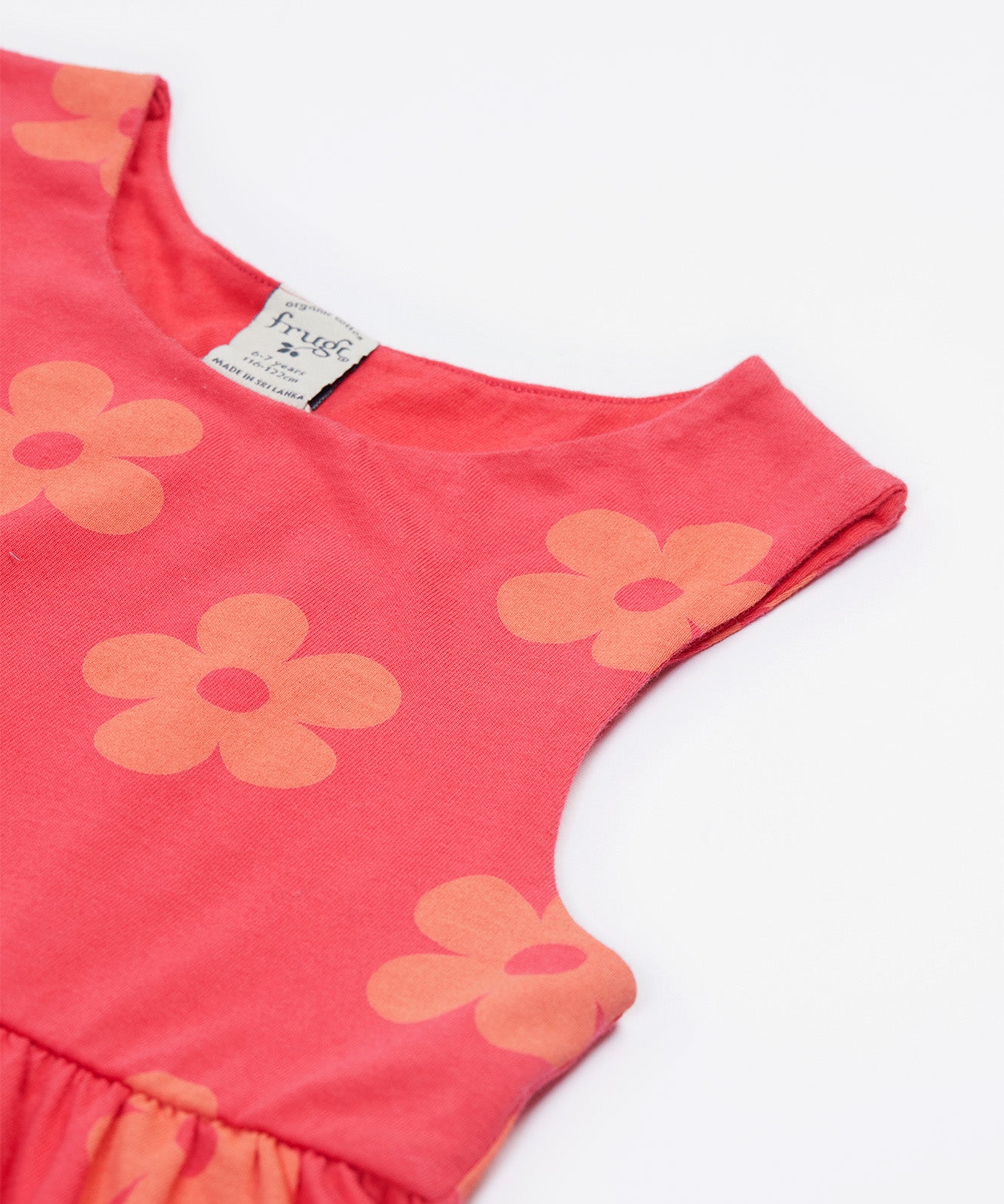 A close up of the Frugi kids summer flamingo / flower dress. Showing the detail neck and sleeve cuffs with the light coral flowers on pink organic cotton fabric