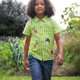 A child wearing the Frugi Green Macaw Gingham  Greengrocer Reggie Shirt with denim shorts.