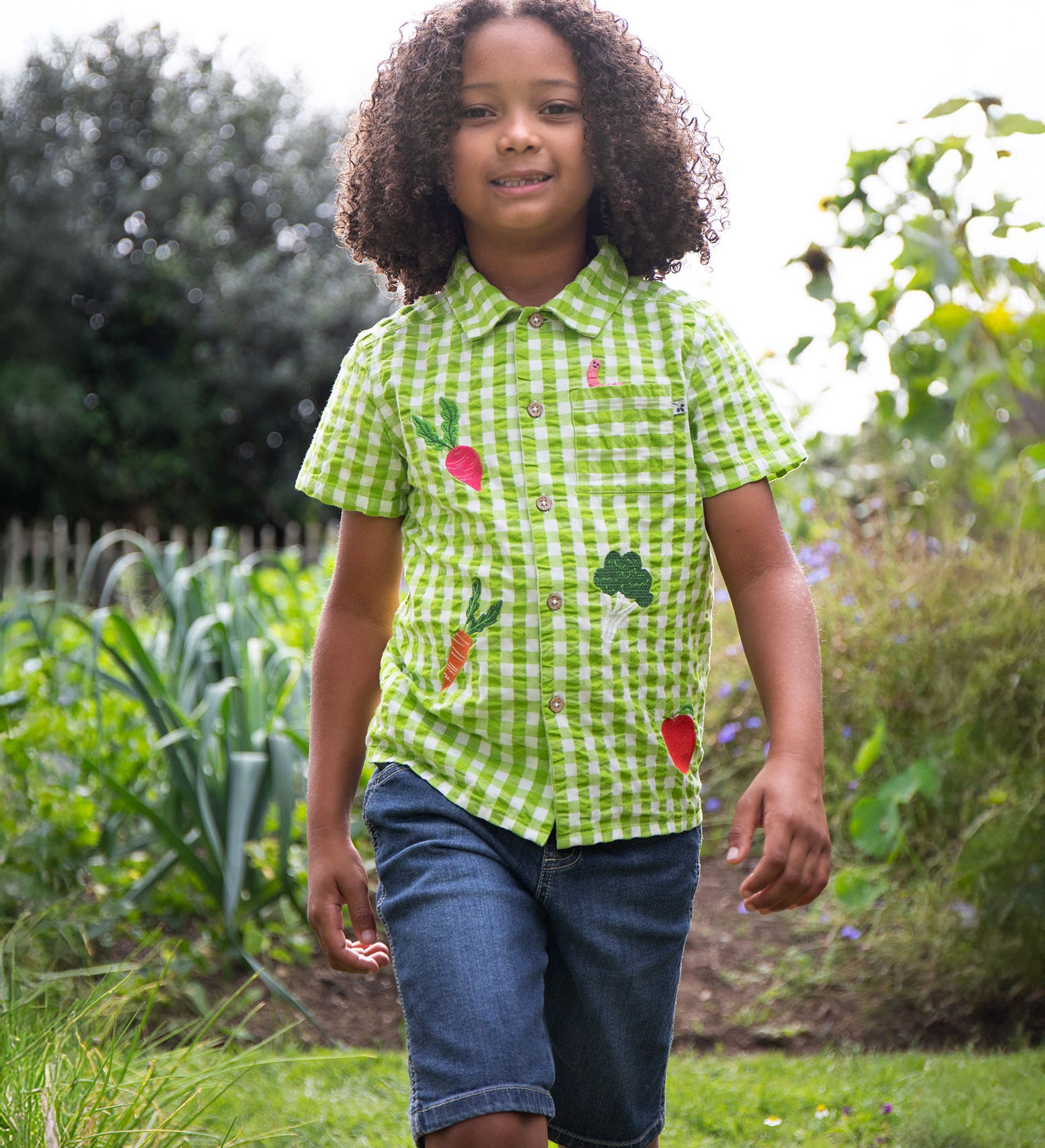 A child wearing the Frugi Green Macaw Gingham  Greengrocer Reggie Shirt with denim shorts.