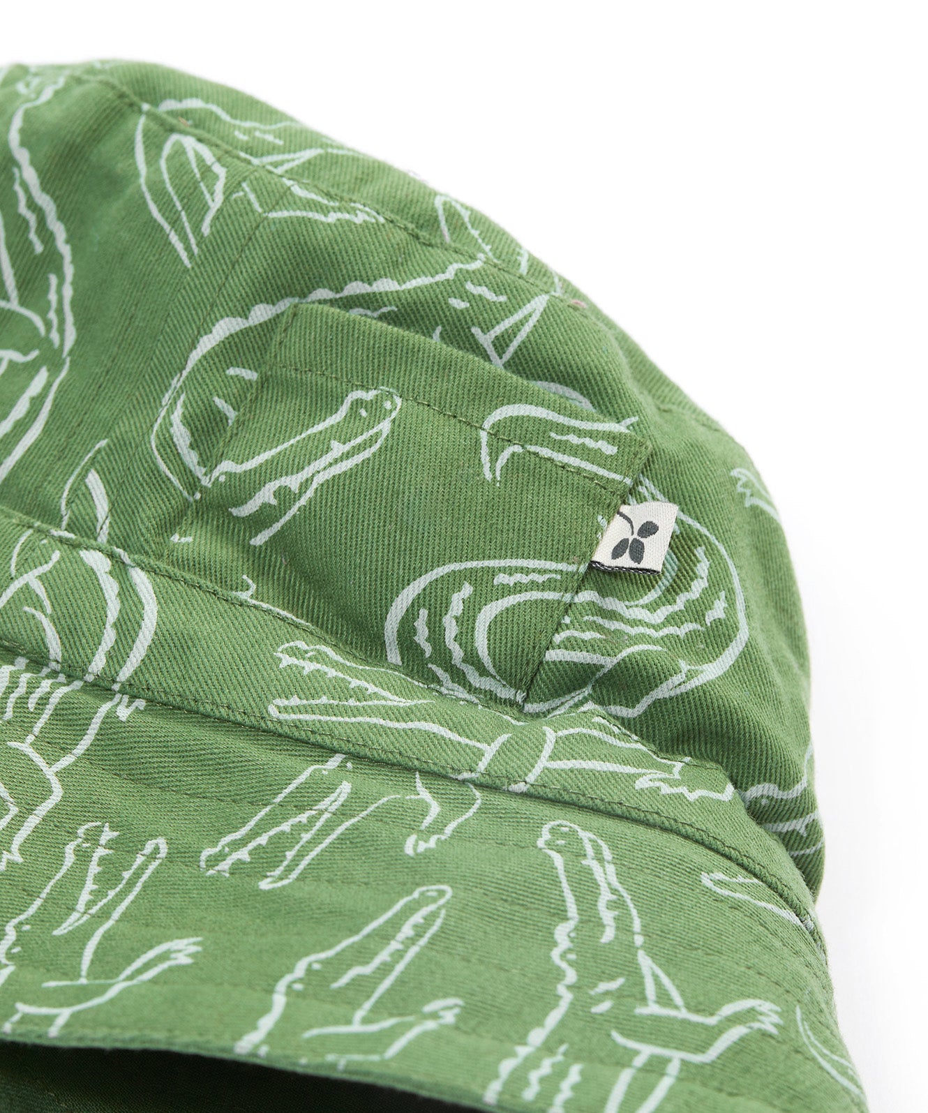 A close up of the Frugi kids green crocodile reversible hat. Showing the little pocket detail on the side of the hat surrounded by the white outlined crocodile design on green organic cotton fabric