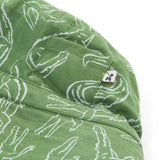 A close up of the Frugi kids green crocodile reversible hat. Showing the little pocket detail on the side of the hat surrounded by the white outlined crocodile design on green organic cotton fabric