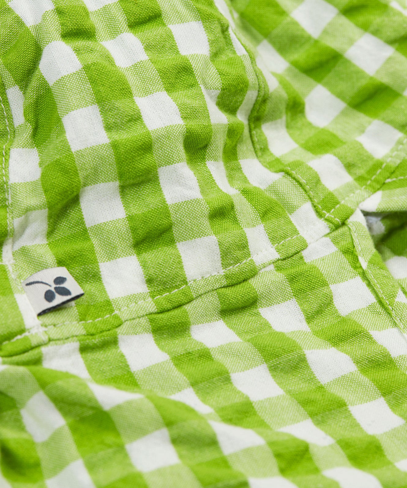 A close up of the Frugi little seersucker sun hat. Showing the stitching between the neck protector and top panel of the hat with the Frugi label on the side on white and green gingham organic cotton fabric