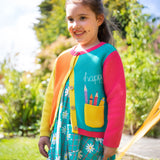 A child wearing the Frugi Happy Pen Pot Rose Pocket Cardigan with a Frugi Floral Check Summer Holiday Dress underneath.