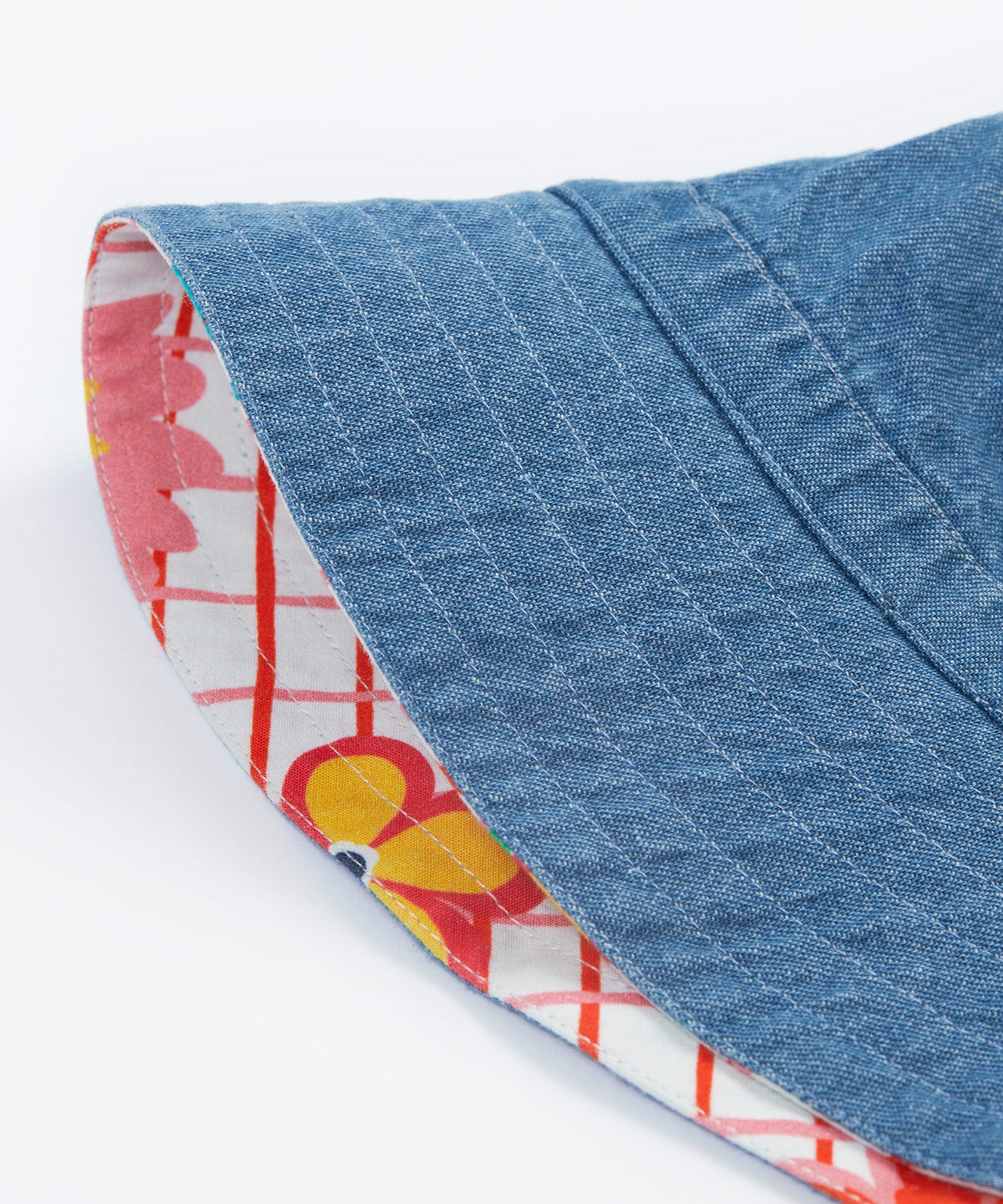 Close up of the Frugi kids hattie reversible hat - showing the denim detail and the white square with red lines and flower design on the flip side of the bucket hat on a organic cotton fabric