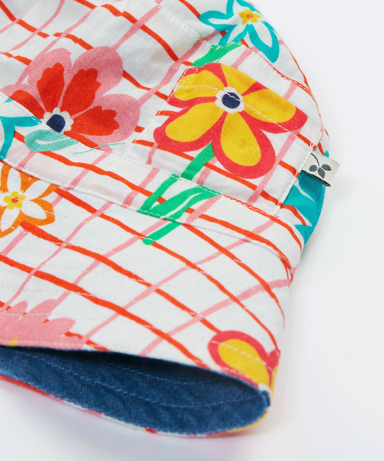 Close up of the Frugi kids hattie reversible hat - showing the white square with red lines and flower design with the denim detail on the flip side of the bucket hat on a organic cotton fabric