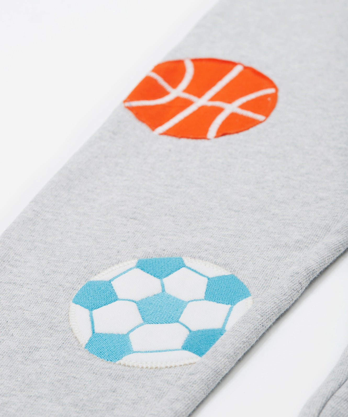 Close up of the Frugi kids jack appliqué joggers. Showing the football and basketball appliqué on grey organic cotton fabric