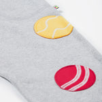 Close up of the Frugi kids jack appliqué joggers. Showing the tennis and cricket ball appliqué on grey organic cotton fabric