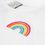 Close up of the Frugi kids jersey rainbow dress - showing a rainbow embroidery on white organic cotton fabric