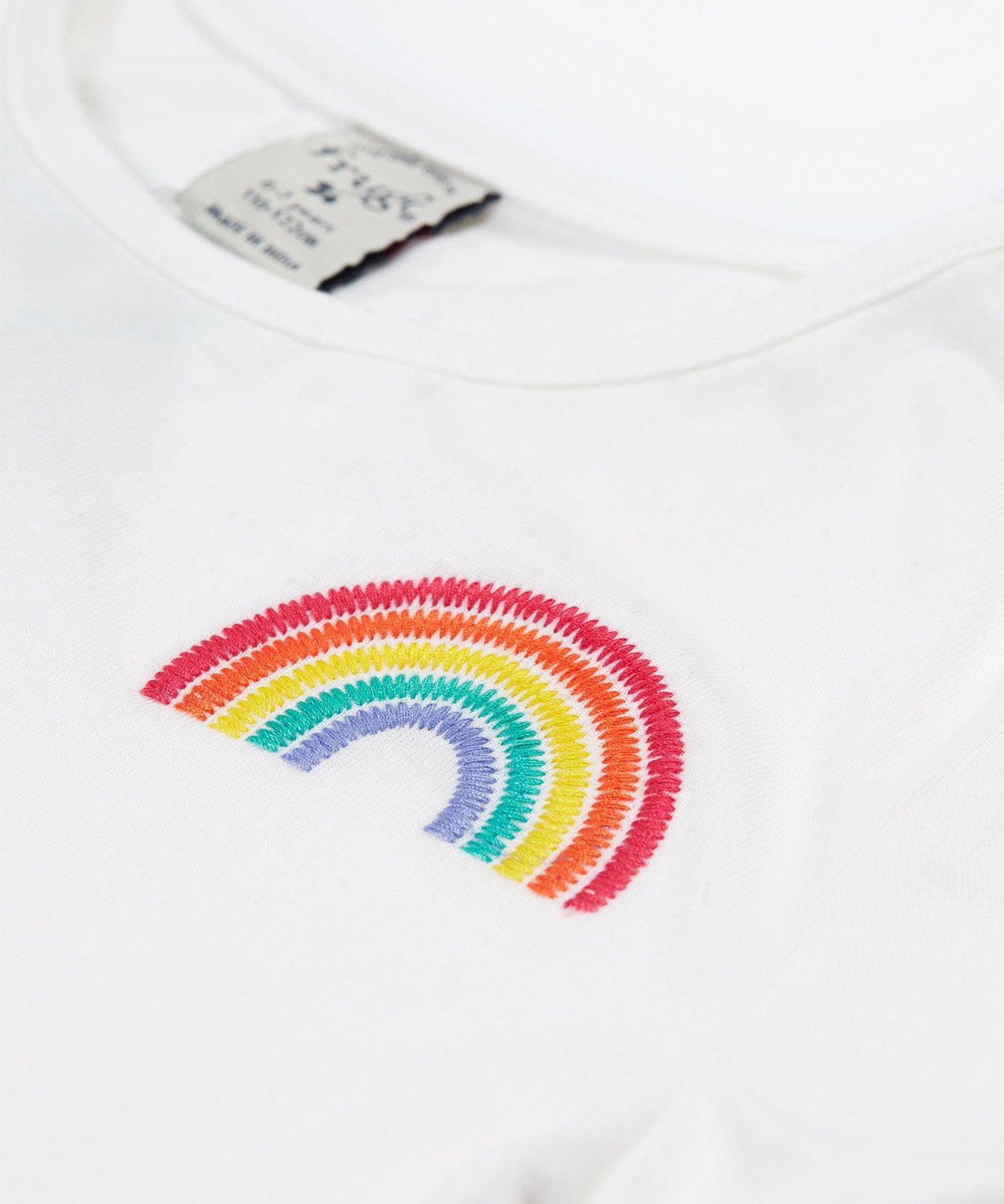 Close up of the Frugi kids jersey rainbow dress - showing a rainbow embroidery on white organic cotton fabric