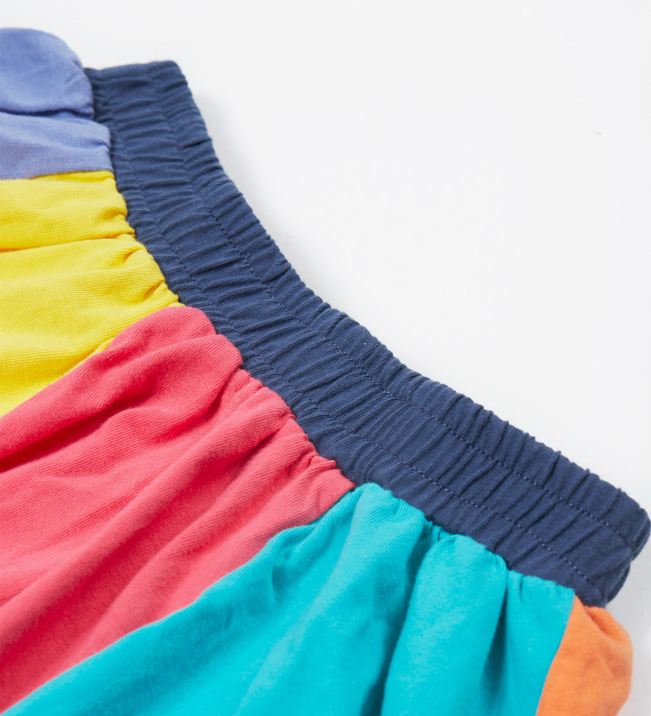 Close up of the Frugi kids rainbow jersey skit showing the navy elasticated waist band and rainbow colour block  panels on organic cotton fabric