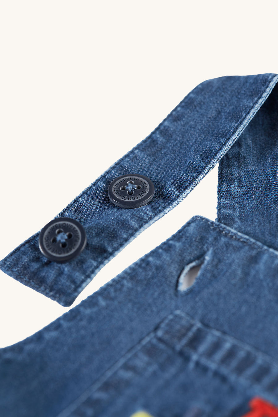 A closer look at the embroidered tractor patch on the front pocket of the Frugi Organic Carnkie Chambray Denim Dungarees - Tractor. Inside the tractor is a lion waving