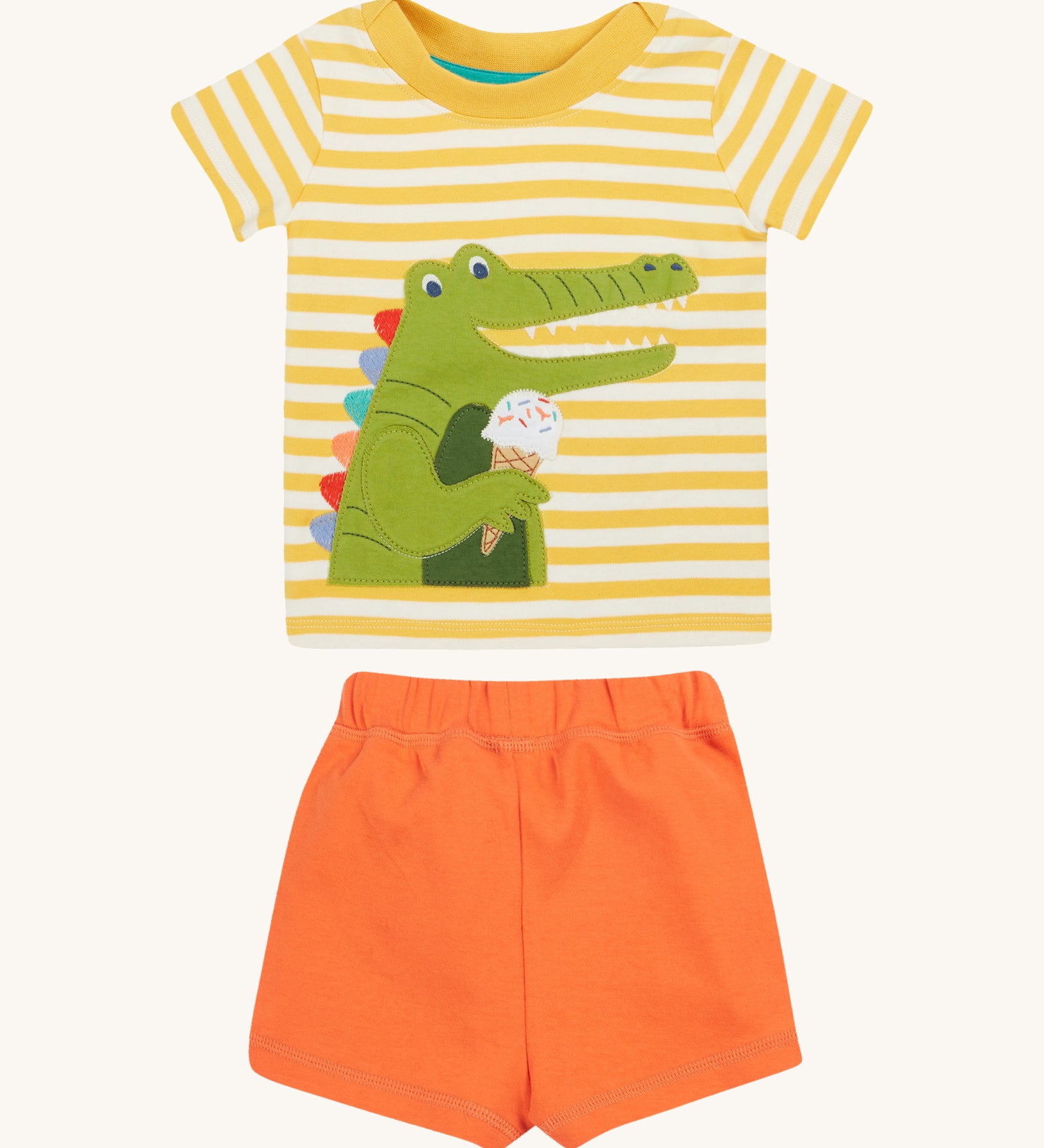 Frugi kids easy wrap around crocodile outfit. GOTS organic cotton Frugi kids outfit with a yellow and white stripe, short sleeve t-shirt, yellow neck trim and orange short. Features a crocodile eating a ice applique on the front of the t-shirt