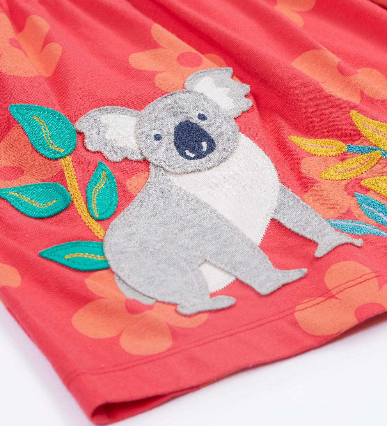 Close up of the Frugi kids flora fun koala tunic top. Showing the appliqué of a grey koala next to bamboo shoots on light pink organic cotton fabric with pastel orange floral prints