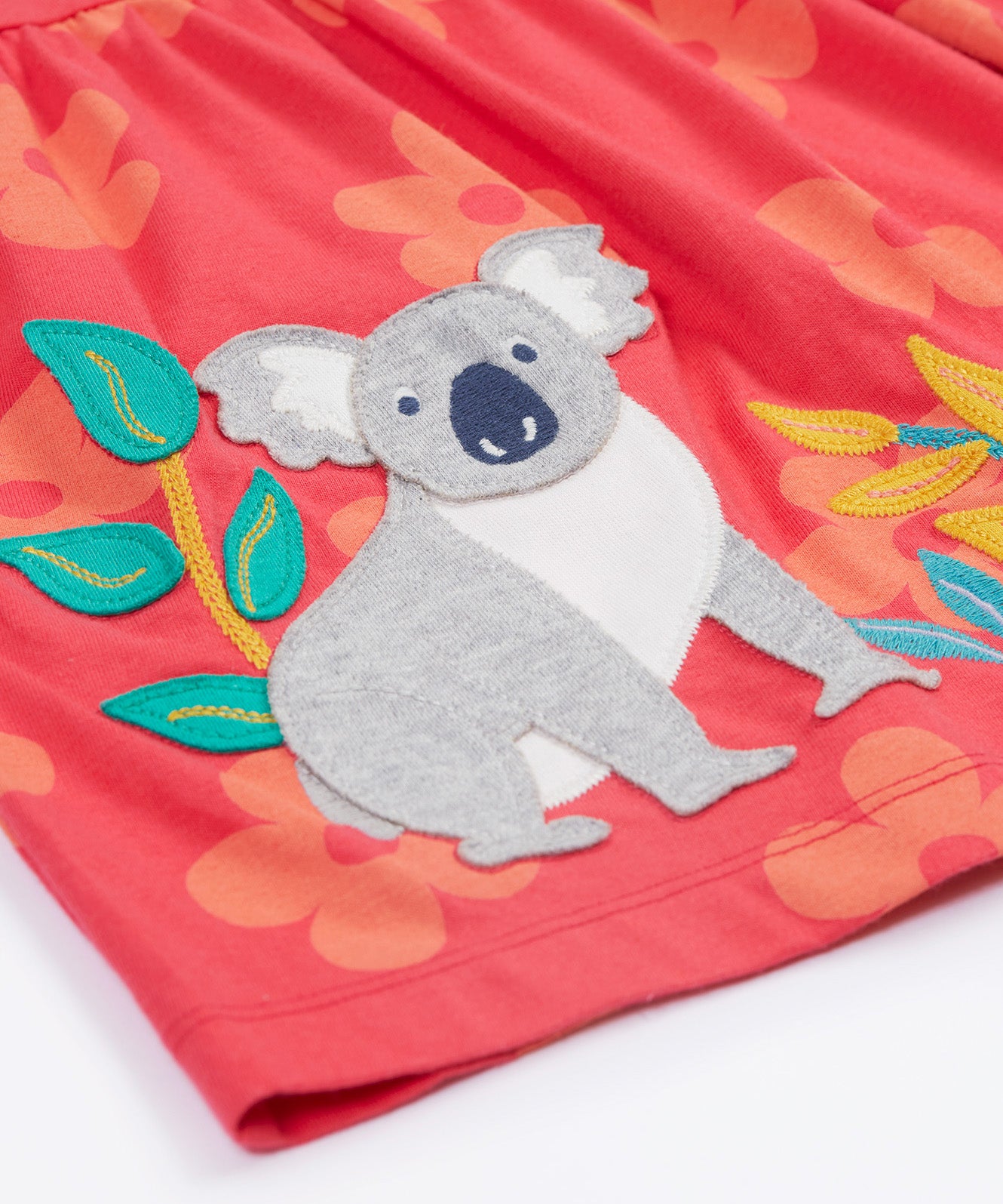 Close up of the Frugi kids flora fun koala tunic top. Showing the appliqué of a grey koala next to bamboo shoots on light pink organic cotton fabric with pastel orange floral prints