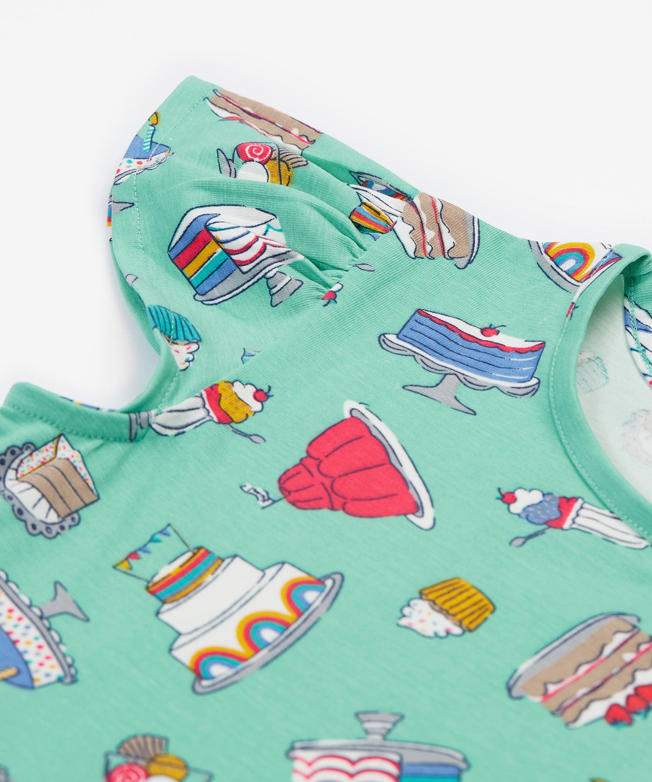 A close up of the Frugi kids lets bake Morwenna skater dress. Showing the different cakes, ice cream, puddings and short sleeve on light green organic cotton fabric