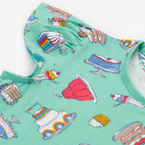 A close up of the Frugi kids lets bake Morwenna skater dress. Showing the different cakes, ice cream, puddings and short sleeve on light green organic cotton fabric