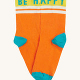 Close up of the Frugi orange sunnie socks. Showing the Be Happy slogan on the ankle cuff. Features a light blue heel and toe contrast panel on orange organic cotton fabric