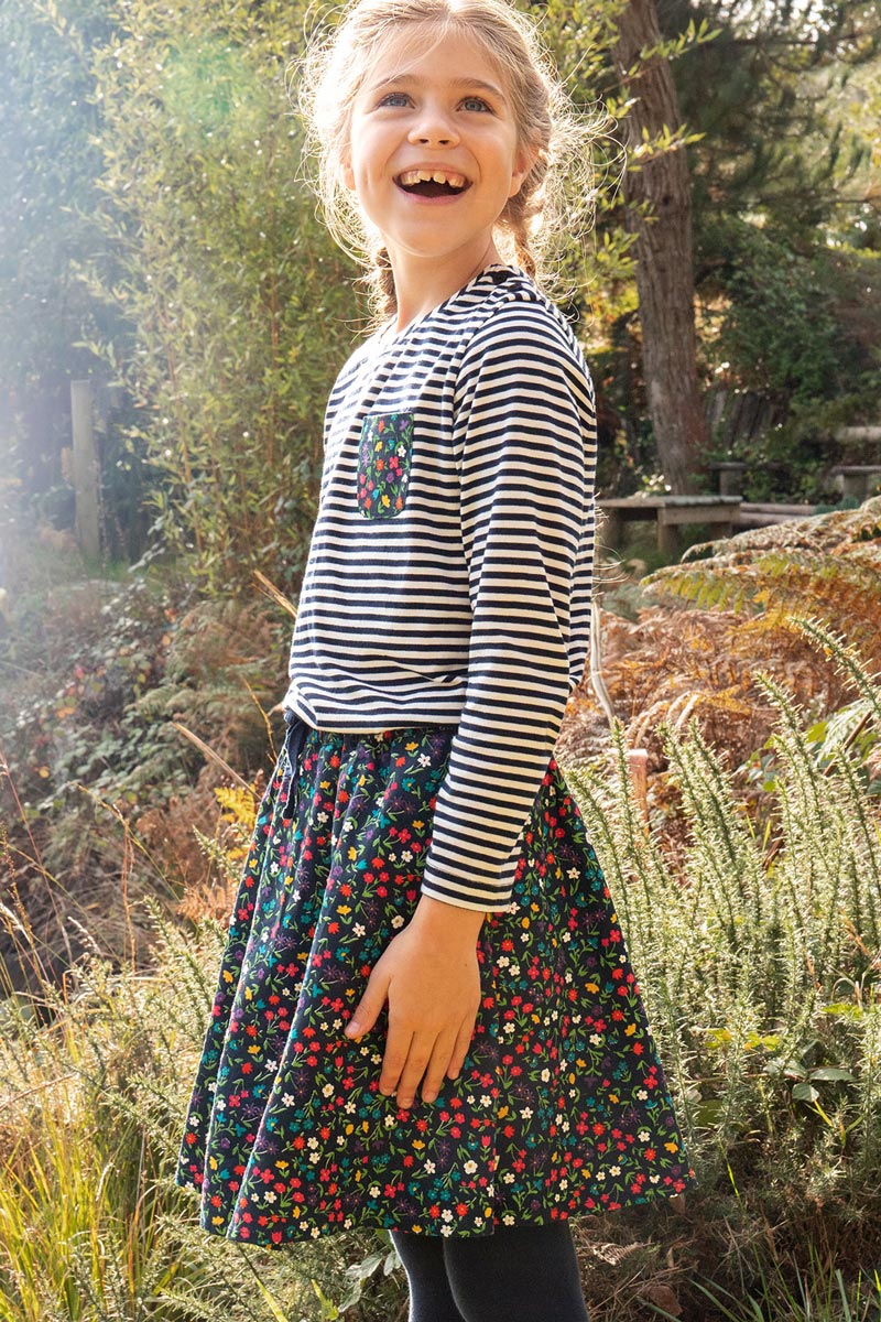 Girl stood in the woods wearing a striped top and the Frugi floral print maeve twill skirt