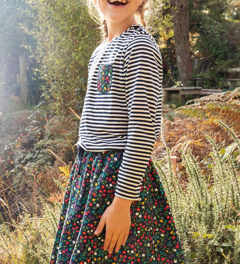 Girl stood in the woods wearing a striped top and the Frugi floral print maeve twill skirt