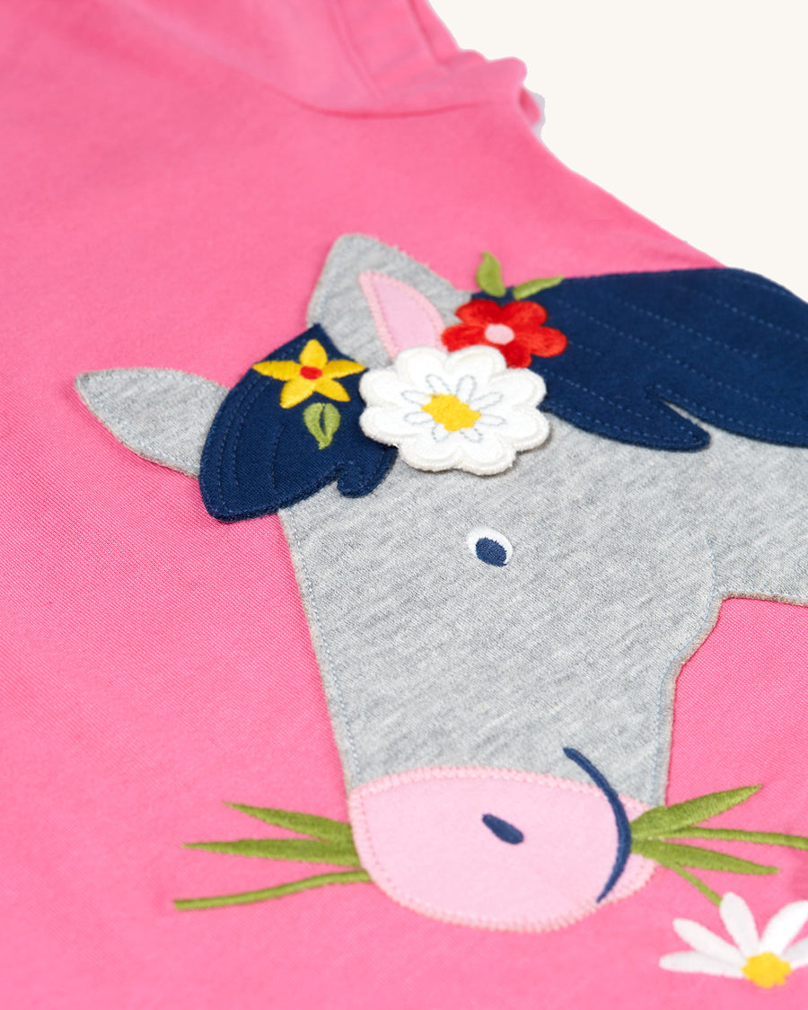 A child happily playing in the sunshine wearing the Frugi Children's Organic Cotton Elise Applique T-Shirt - Horse. A pink t-shirt with cap sleeves and gorgeous applique horse and flower detailing and soft rib neck