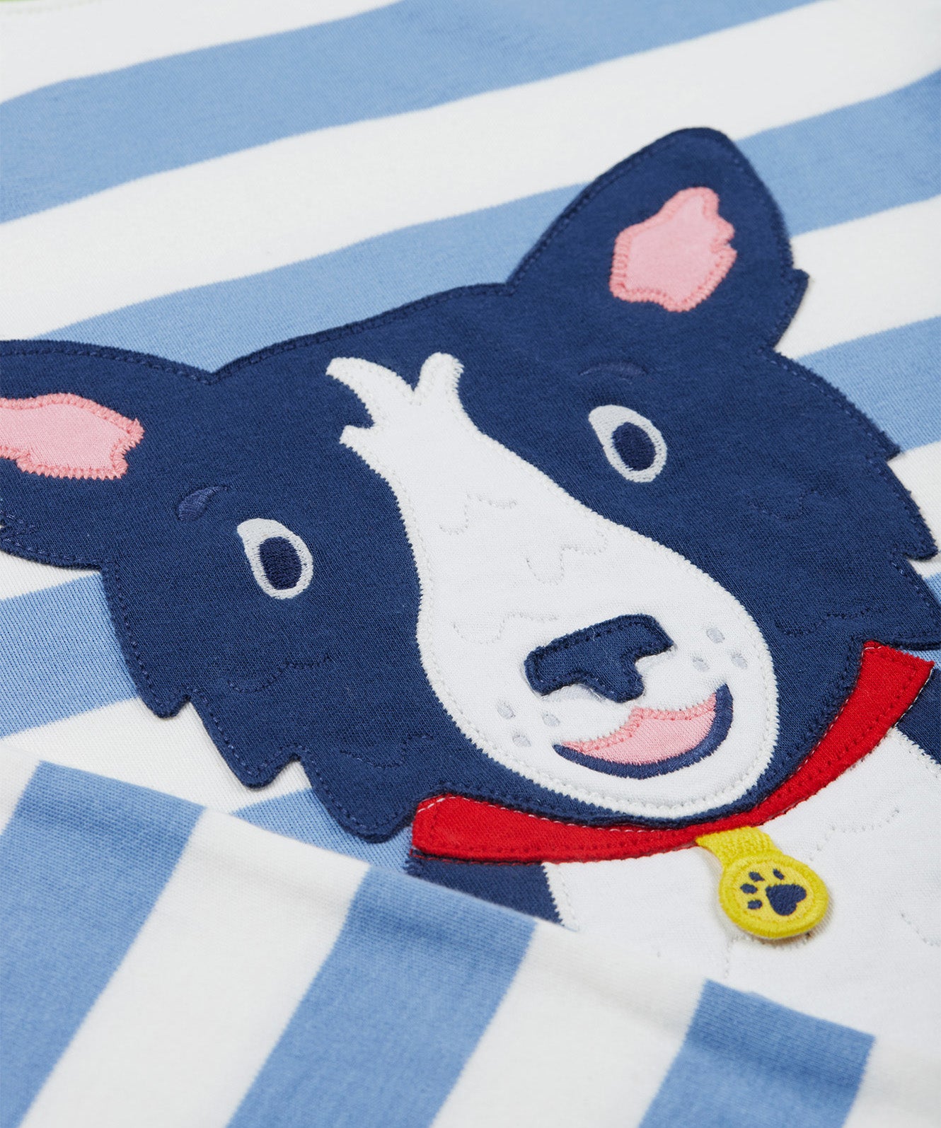 A close up of the Frugi kids Porth collie dog pyjama set showing the appliqué of a collie dog on blue and white striped organic cotton fabric