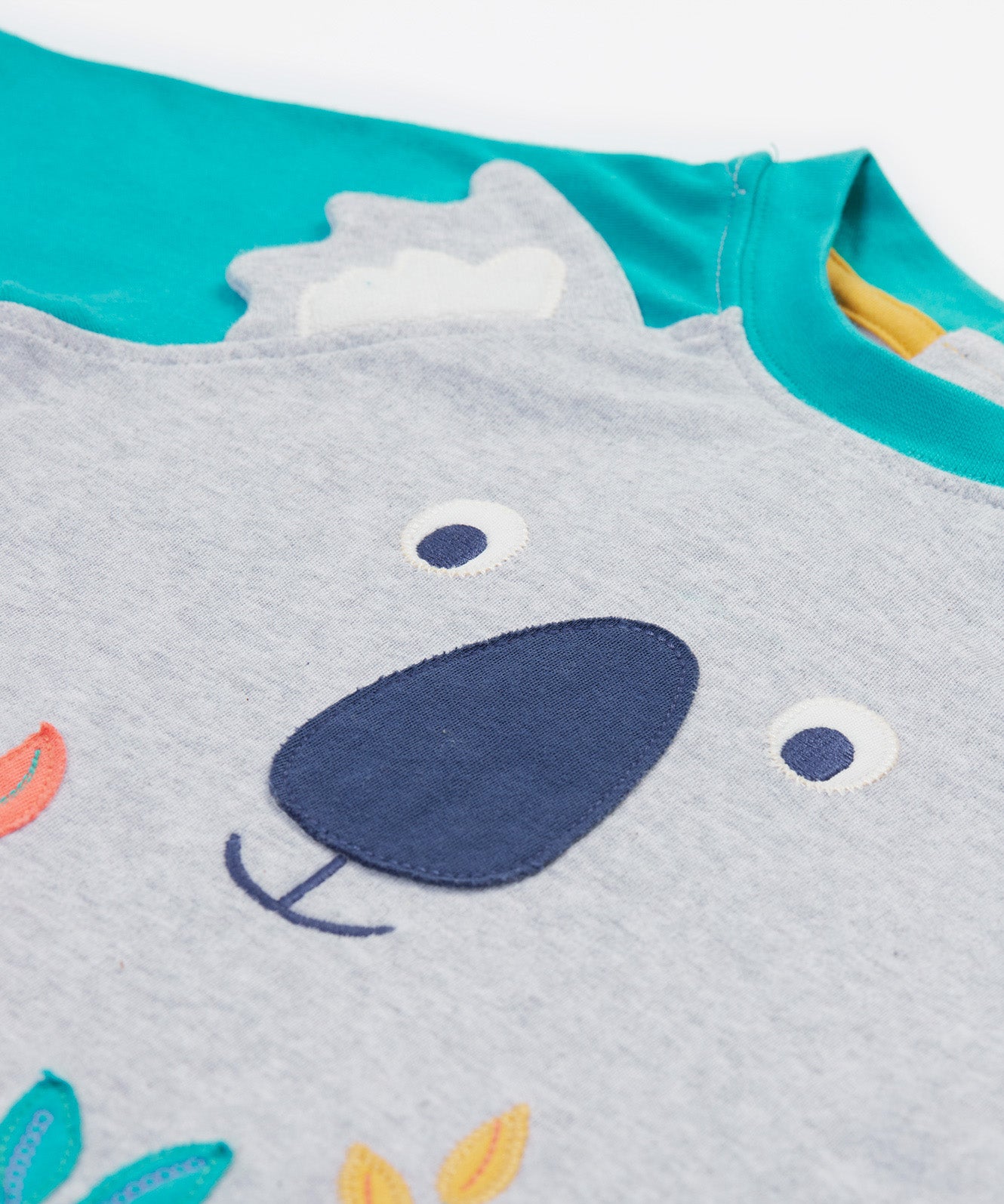 Close up of the Frugi kids koala raglan t-shirt. Showing the grey koala facial features and grey ears stitched loosely on the front panel on grey and blue organic cotton fabric