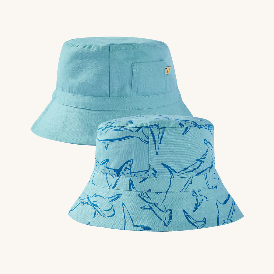 Frugi Children's Organic Cotton Rocky Reversible Hat - Stingray / Jawsome. A fun, reversible sun hat in light blue. On one side of the hat are beautiful shark prints, and the reversible side is plain with a small pocket/pouch with a small Frugi logo label