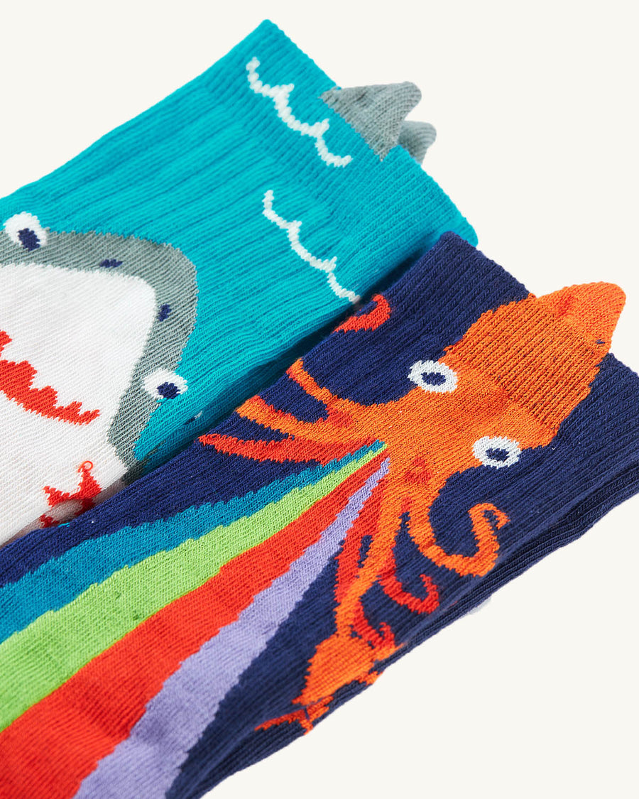  made with GOTS Organic Cotton. A two pair pack of knitted character socks with fun 3D detail. The left pair of socks are of an orange squid shooting rainbow squid ink