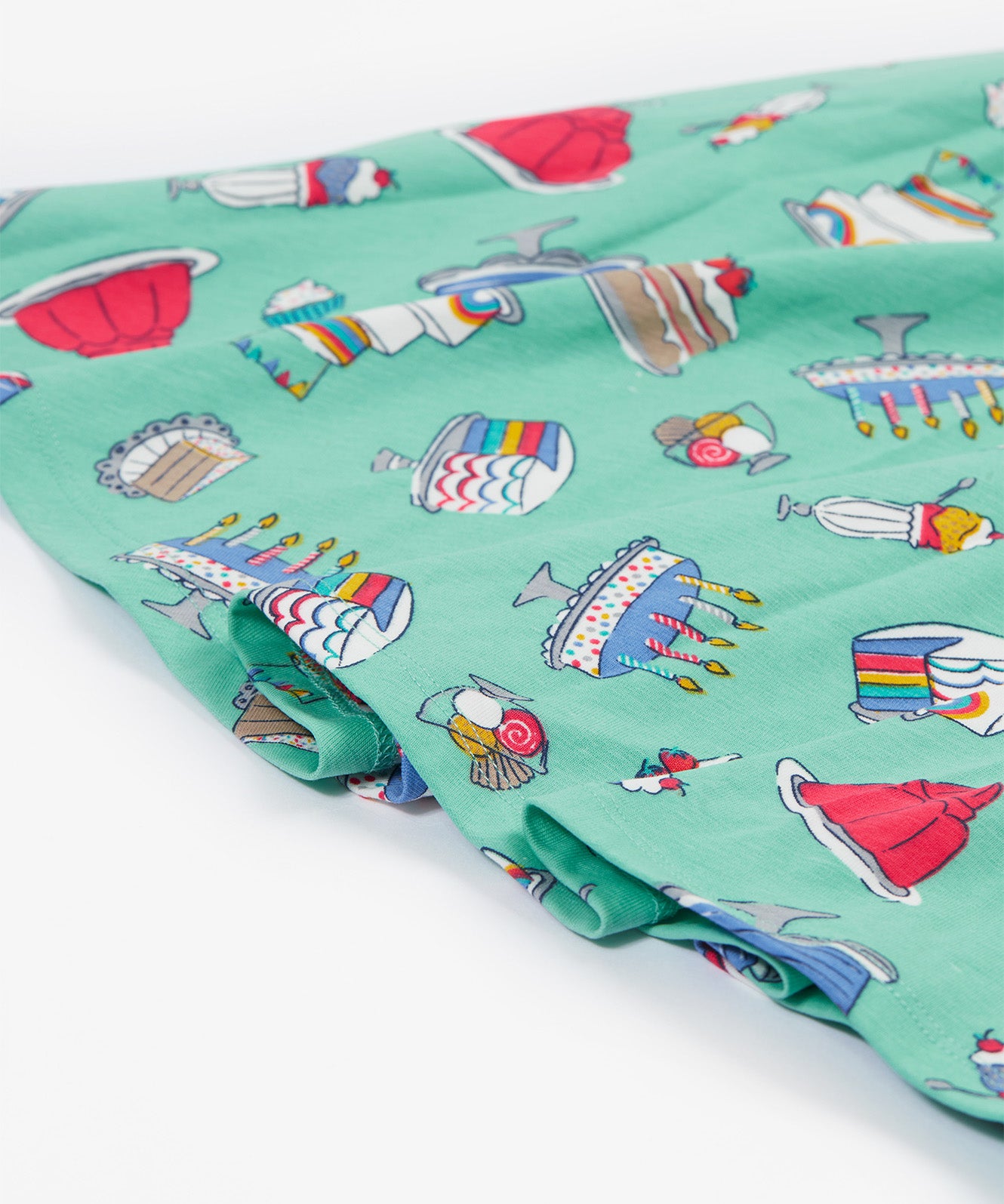 A close up of the Frugi kids lets bake Morwenna skater dress. Showing the different cakes, ice cream, puddings and light frill on light green organic cotton fabric