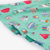 A close up of the Frugi kids lets bake Morwenna skater dress. Showing the different cakes, ice cream, puddings and light frill on light green organic cotton fabric