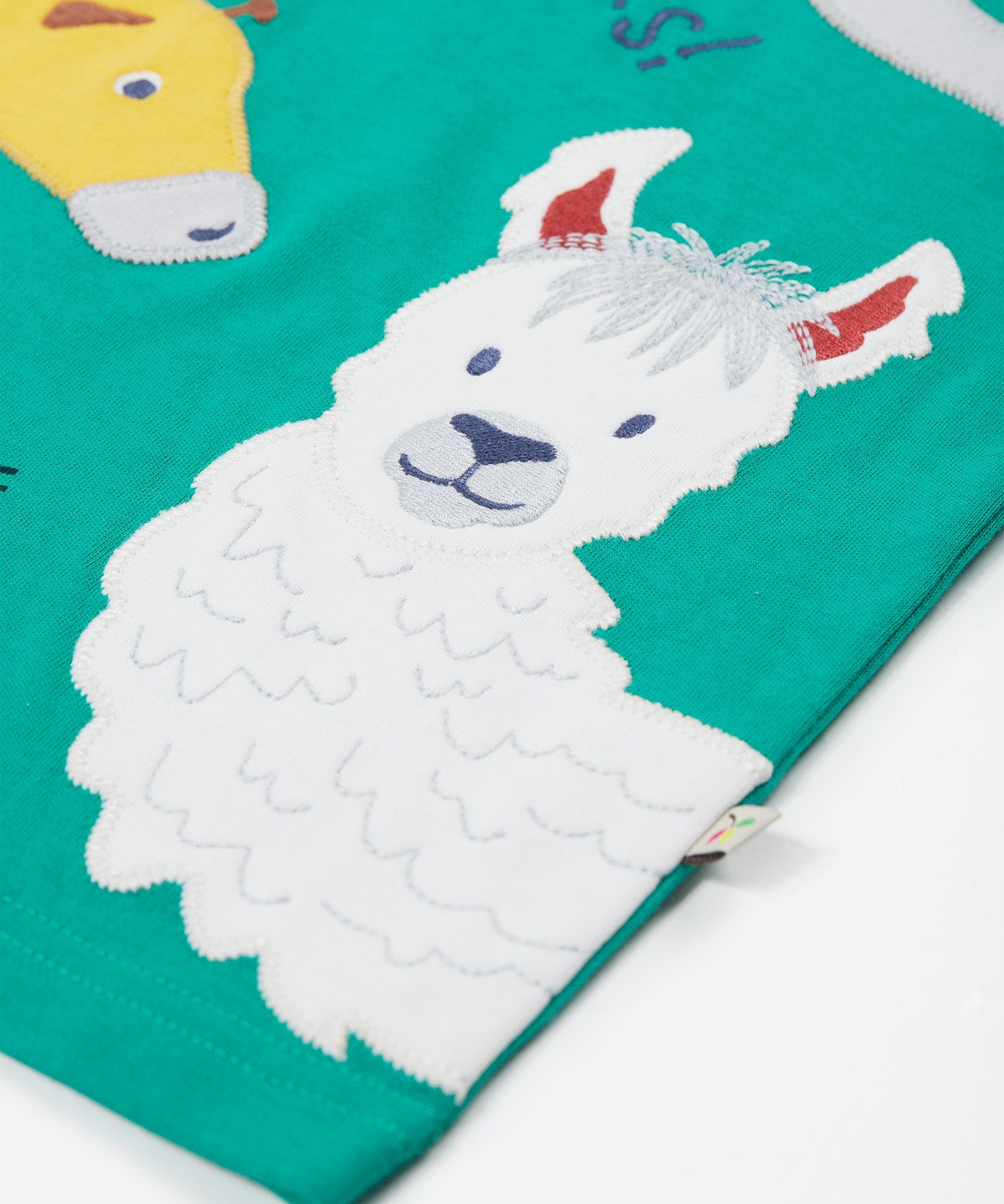 A close up of the Frugi kids long neck pals t-shirt. Showing the white and grey llama appliqué on green organic cotton fabric