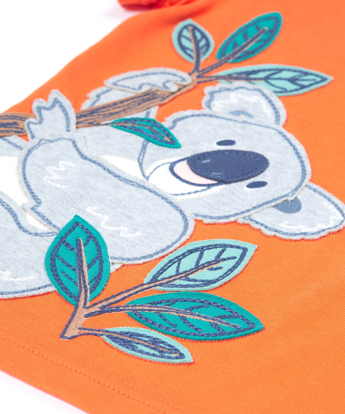 Close up of the Frugi kids orange koala t-shirt. Showing the grey koala applique hanging on embroidered bamboo shoots on light orange organic fabric