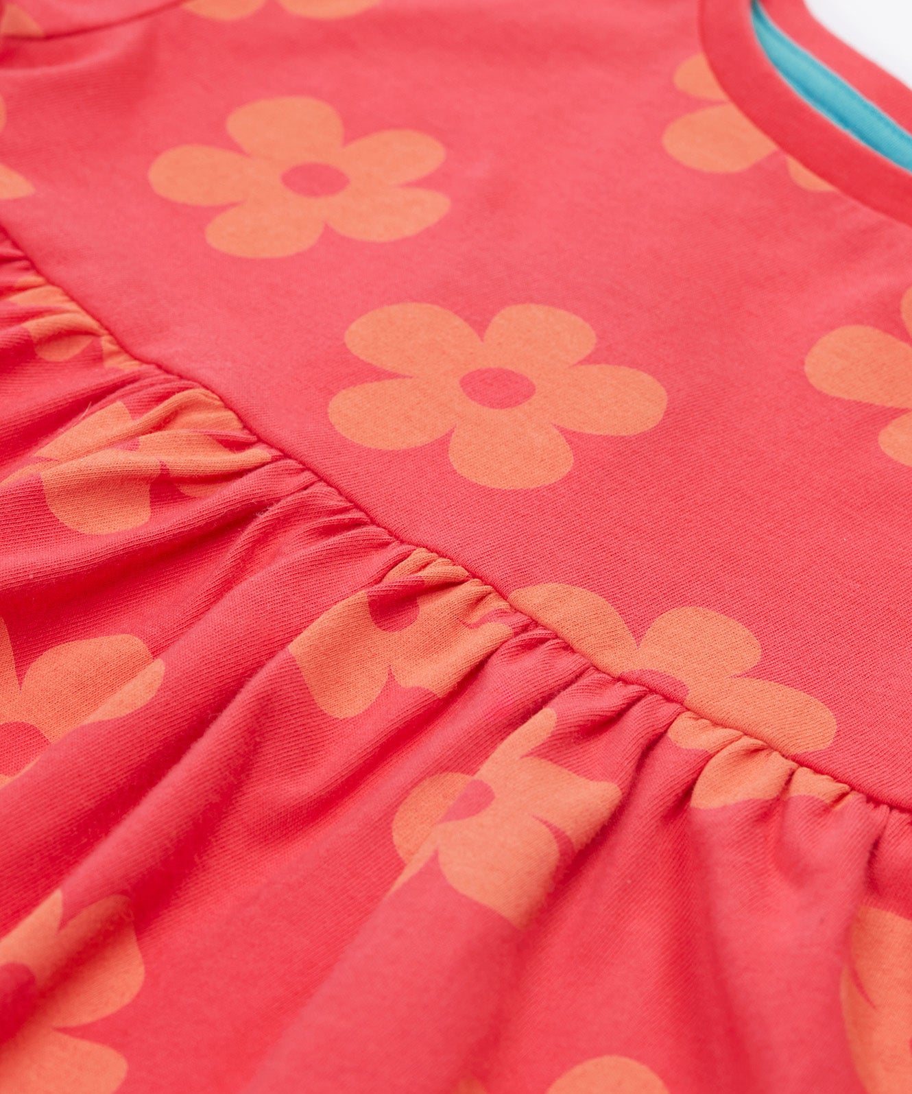 Close up of the Frugi kids flora fun koala tunic top. Showing the stitching detail between the two halves of the tunic top on light pink organic cotton fabric with pastel orange floral prints