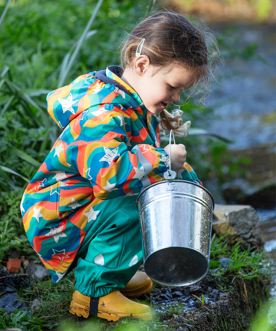 A child pouring water from a metal bucket into a stream