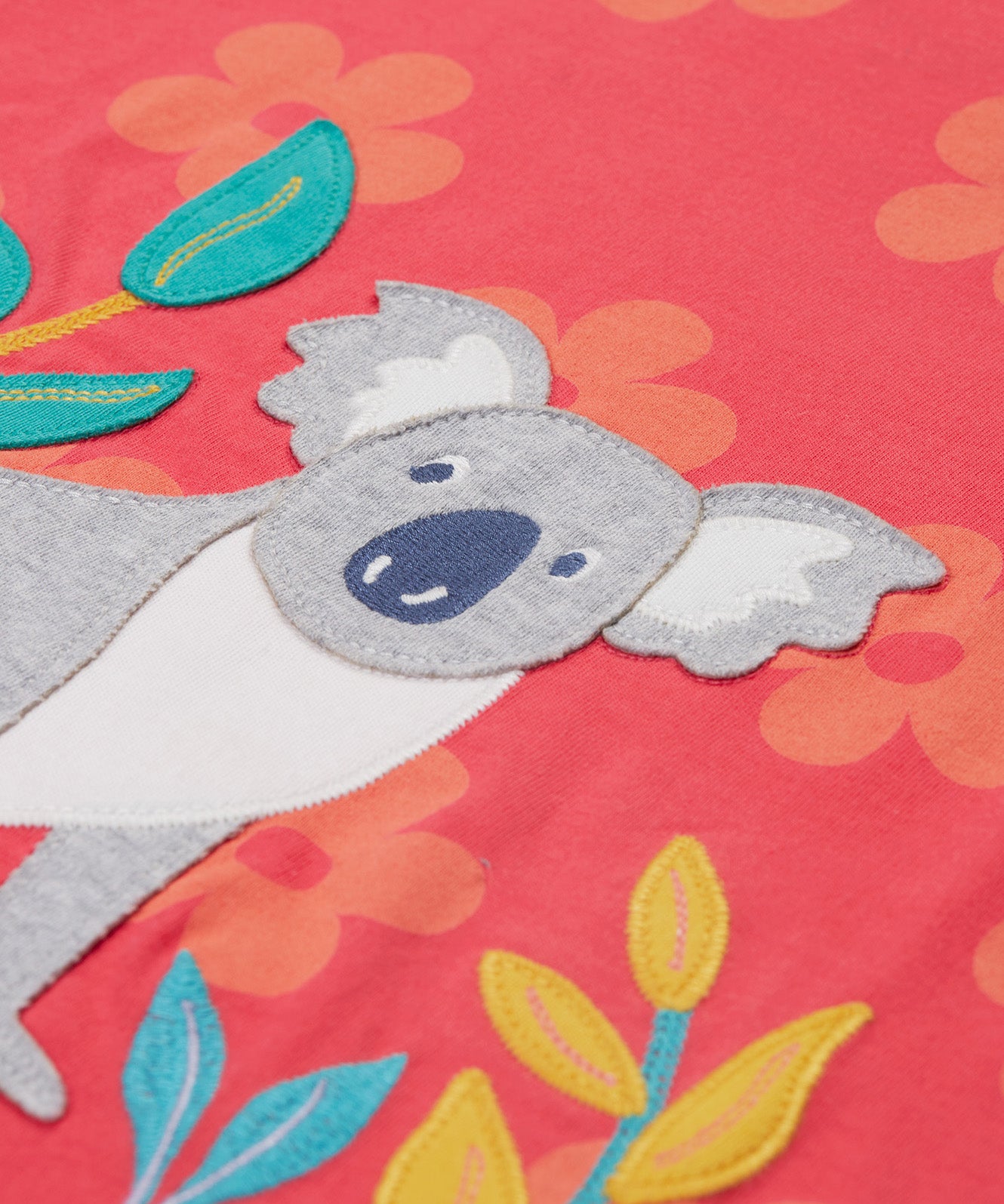 Close up of the Frugi kids flora fun koala t-shirt. Showing the appliqué detail of the grey koala next to 3 bamboo shoots on light pink organic cotton fabric with pastel orange floral prints