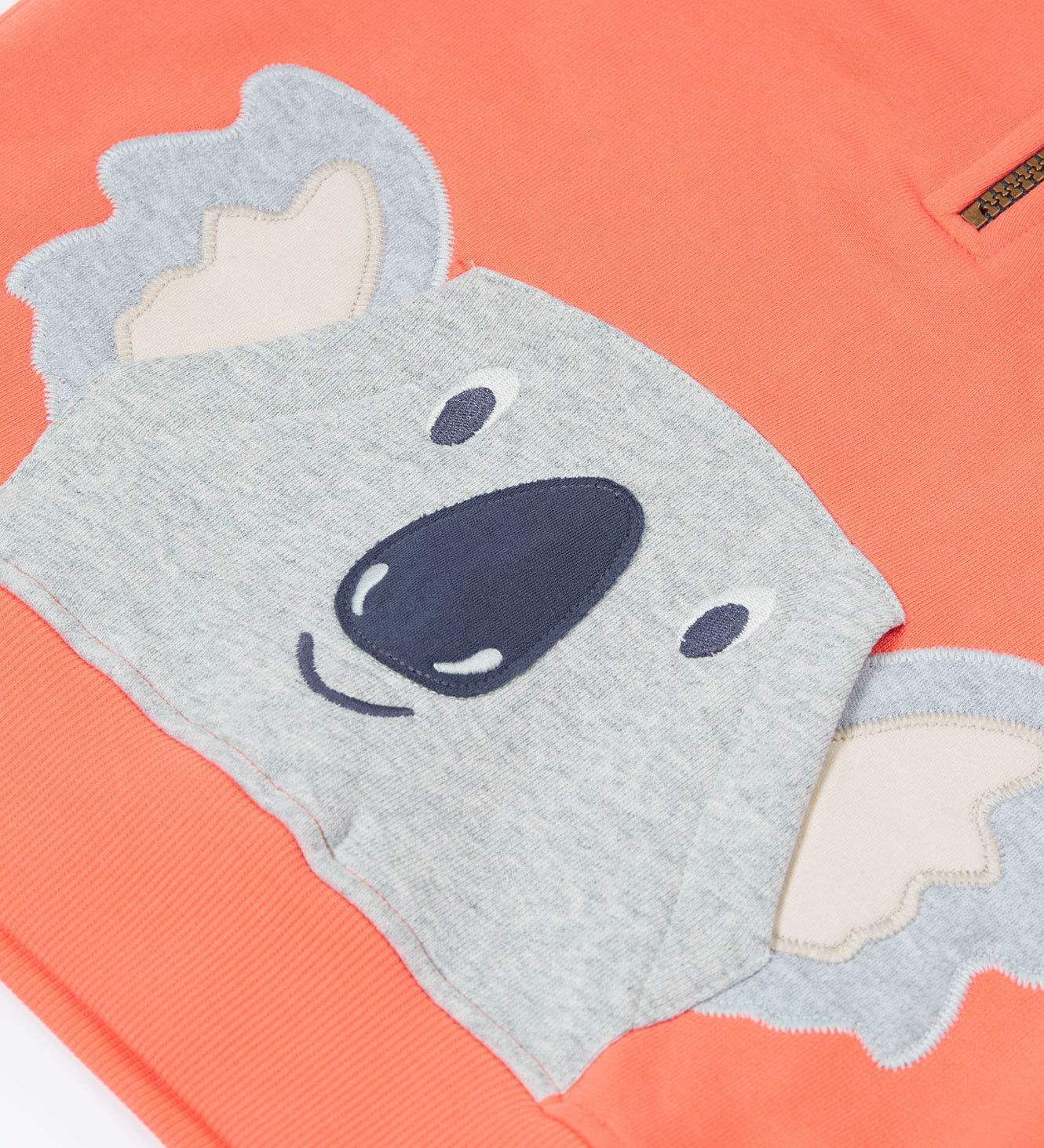 Close up of the Frugi kids koala half zip hoodie showing the appliqué of a grey koala head on coral organic cotton fabric